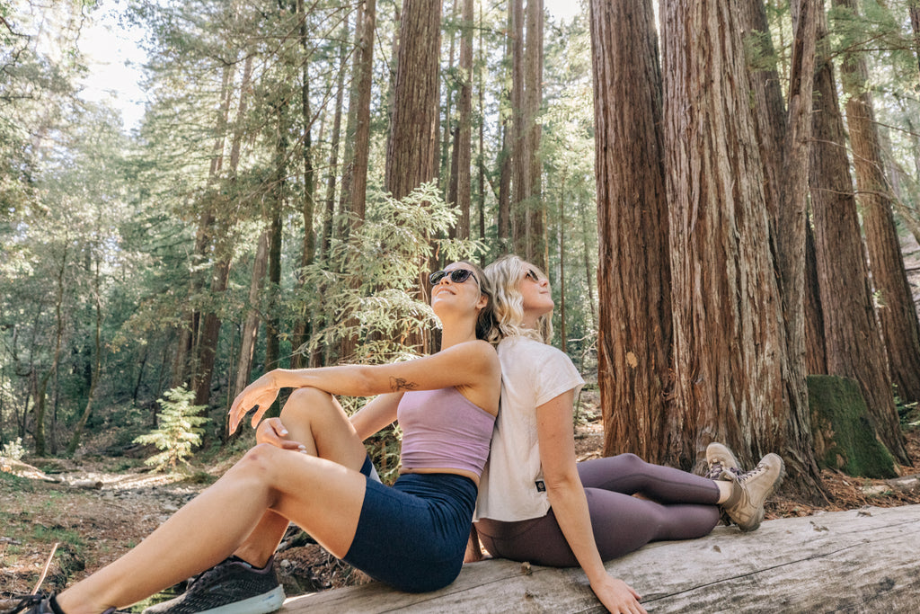 two women in the forest sitting back to back on a log