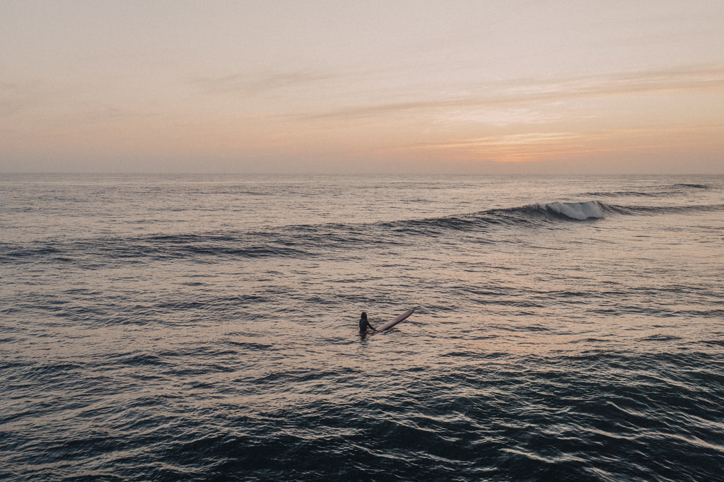 Sunset over the ocean with a lone surfer on the water