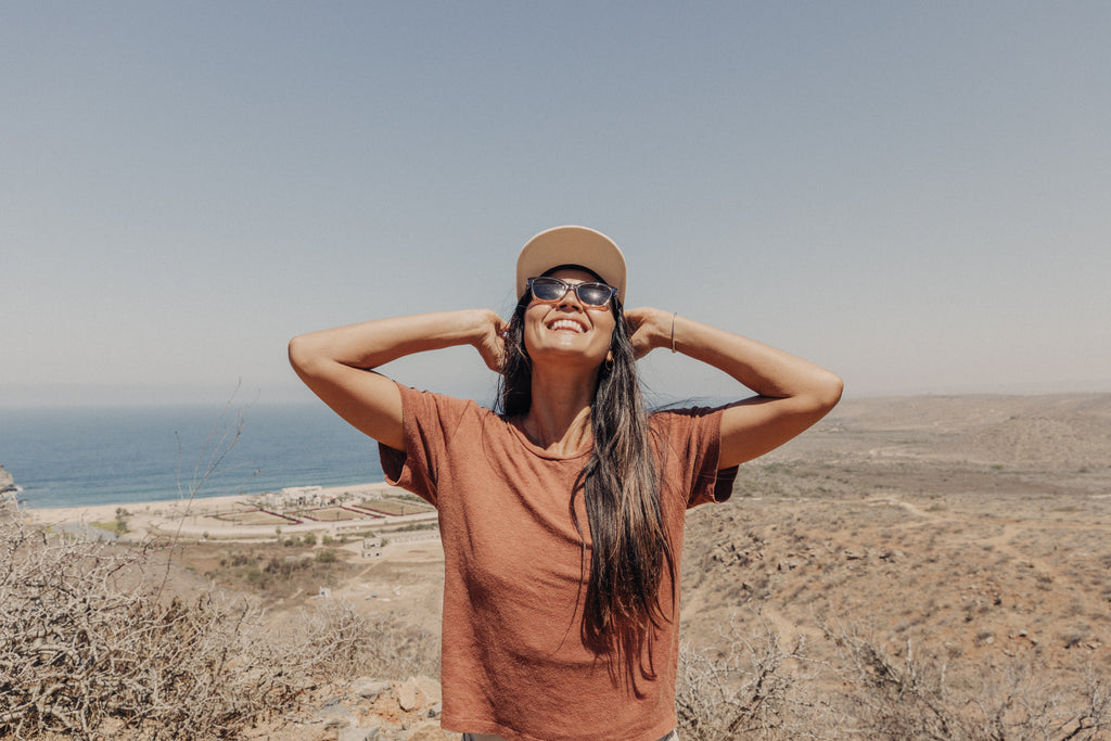 Woman smiling with her hands behind her head and an ocean view