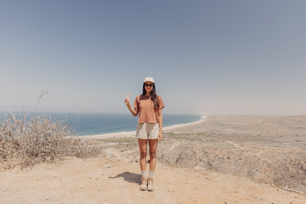 woman wearing recycled sunglasses while holding up a peace sign in front of the ocean