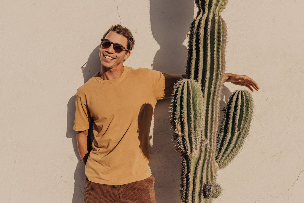 man wearing sustainable sunglasses while hugging a cactus