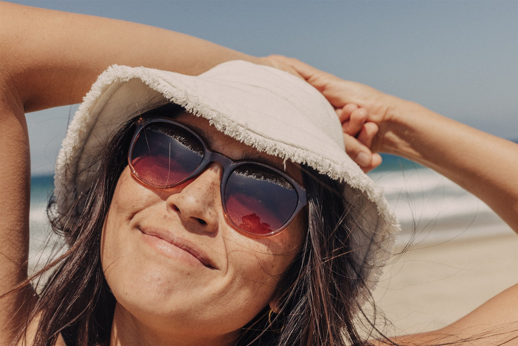 Smiling by the ocean, in sunglasses and hat