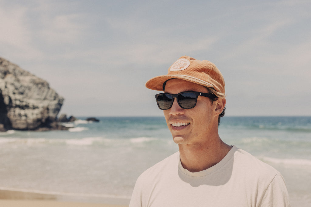 Guy smiling in a hat and sunglasses on the beach