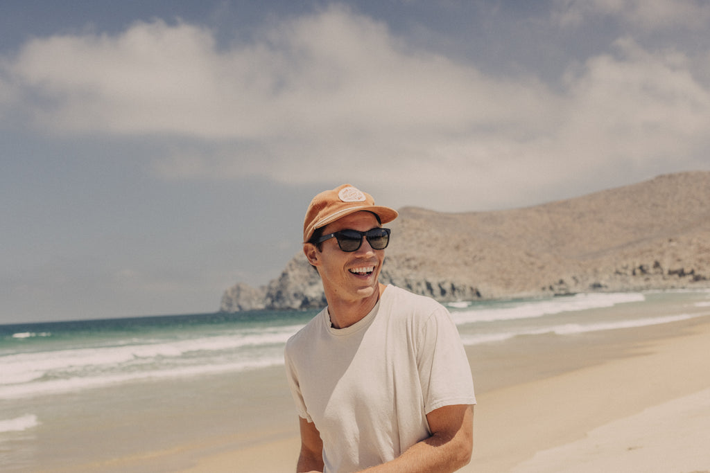 man wearing a pair of sustainable sunglasses while laughing at the beach