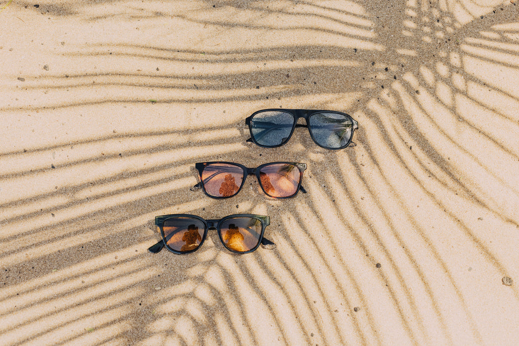 Blue, orange, and pink sunglasses laid out in the sand
