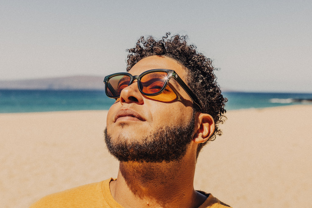 Man basking in the sun on the beach with lo light Sunski sunglasses on