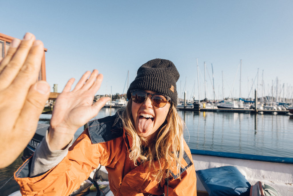 Women in sunglasses and beanie high fives her fishing partner at the dock