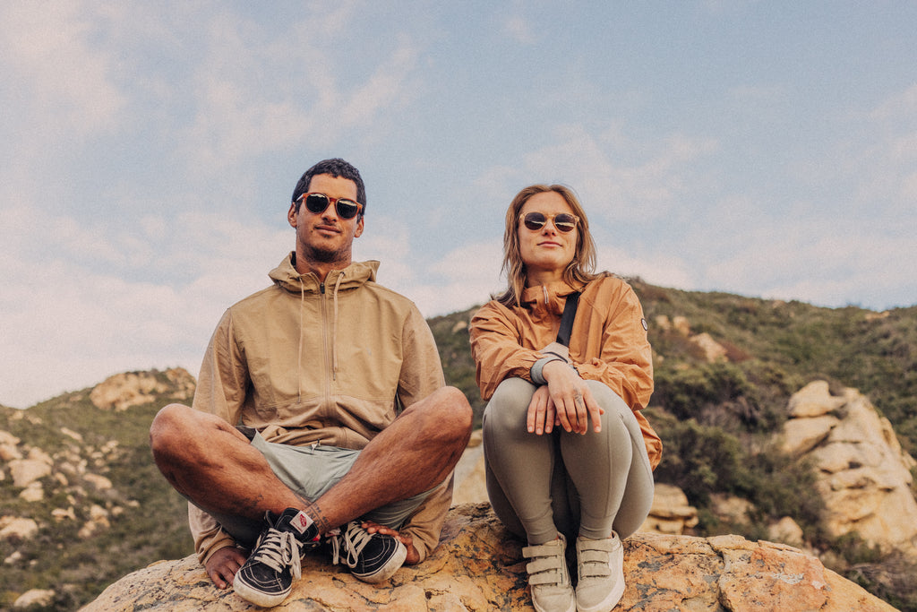 Man and woman sitting next to each other on a rock below the cliffs