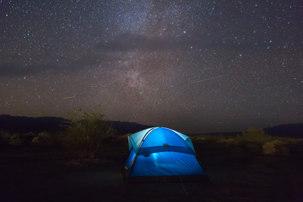 Blue tent illuminated at night against a starry desert