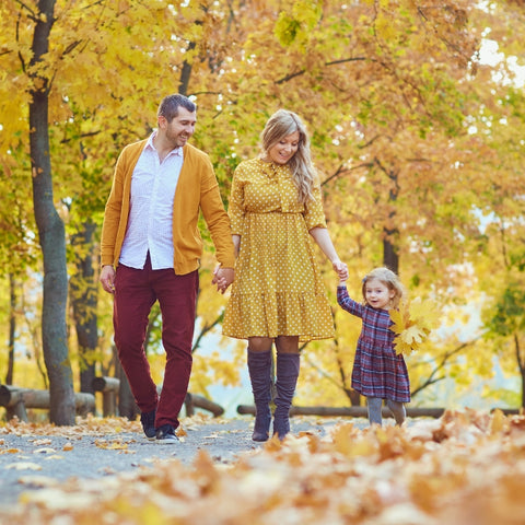 A family of three walking in a park during autumn.