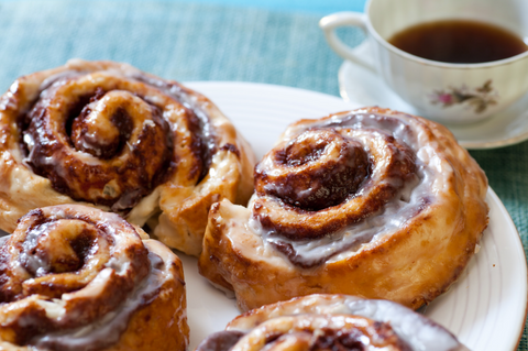 Sweet Vienna style cinnamon rolls with vanilla cream cheese icing on a plate next to a cup of hot cinnamon coffee.