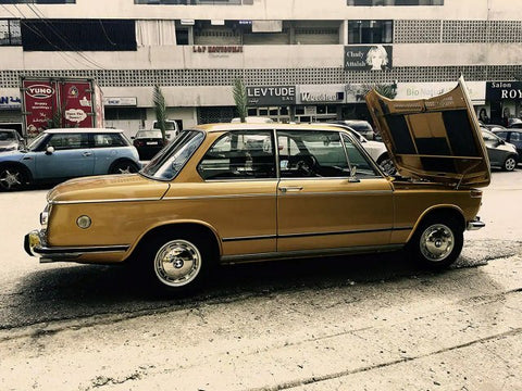 Gold-colored BMW E10 2002, showcasing its classic design with a boxy shape, round headlights, and distinctive kidney grille. The image highlights the car's vintage charm and eye-catching color.