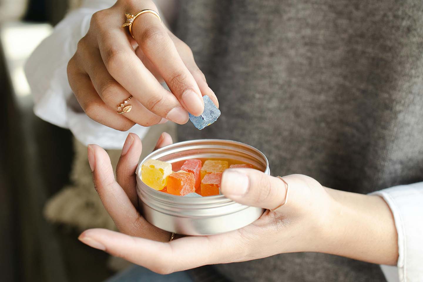 a person holding a tin can of gummies in one hand and picking a blue gummy on another hand