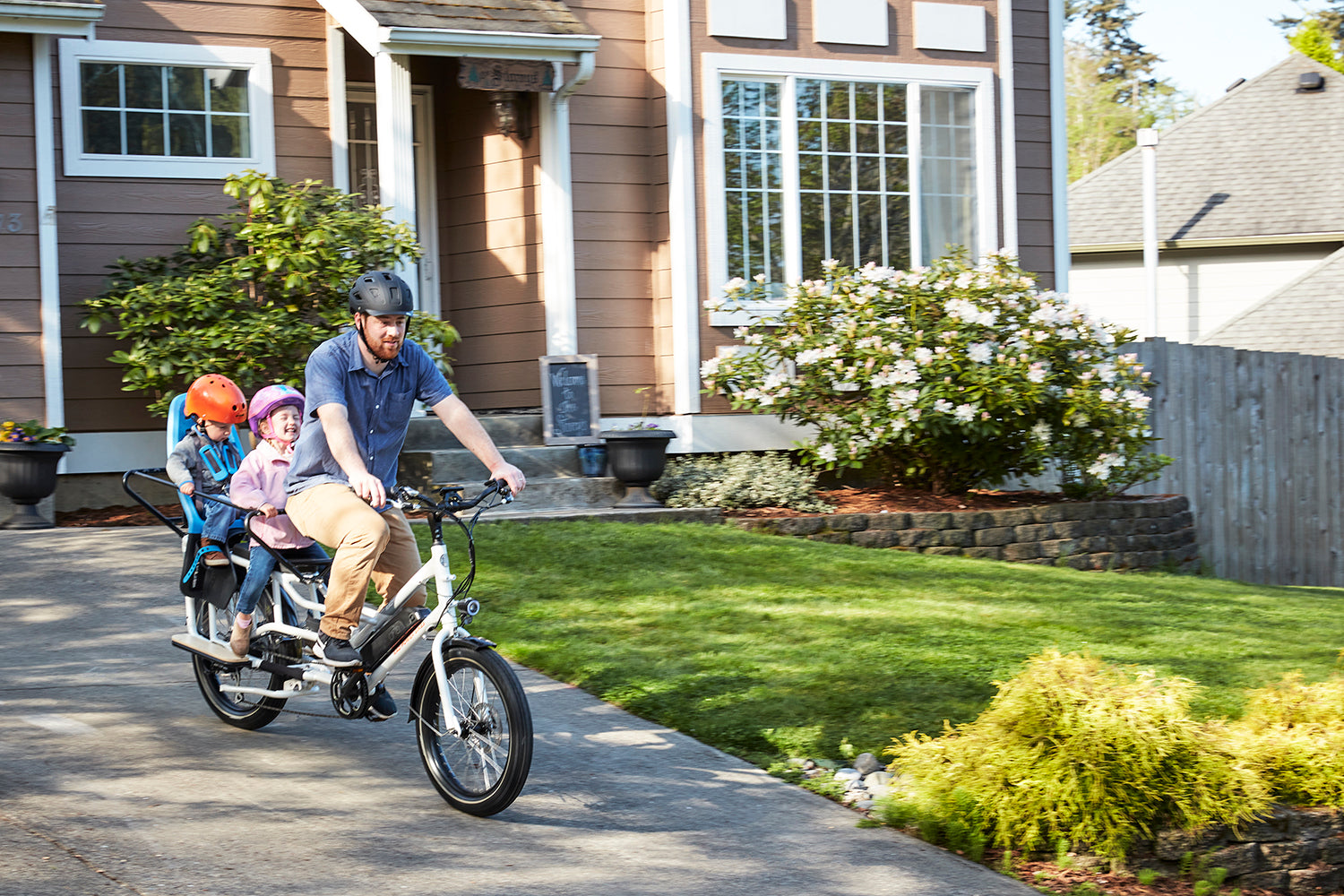 A father rides a RadWagon electric cargo bike with his children out of his driveway.