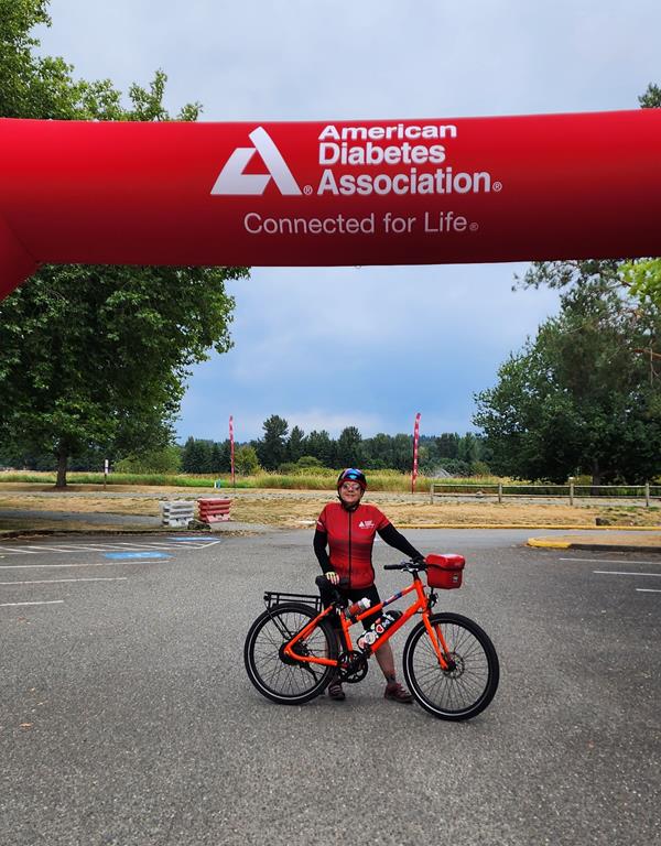 A woman wearing red cycling gear poses with a red Rad electric bike under a fundraising ride banner.