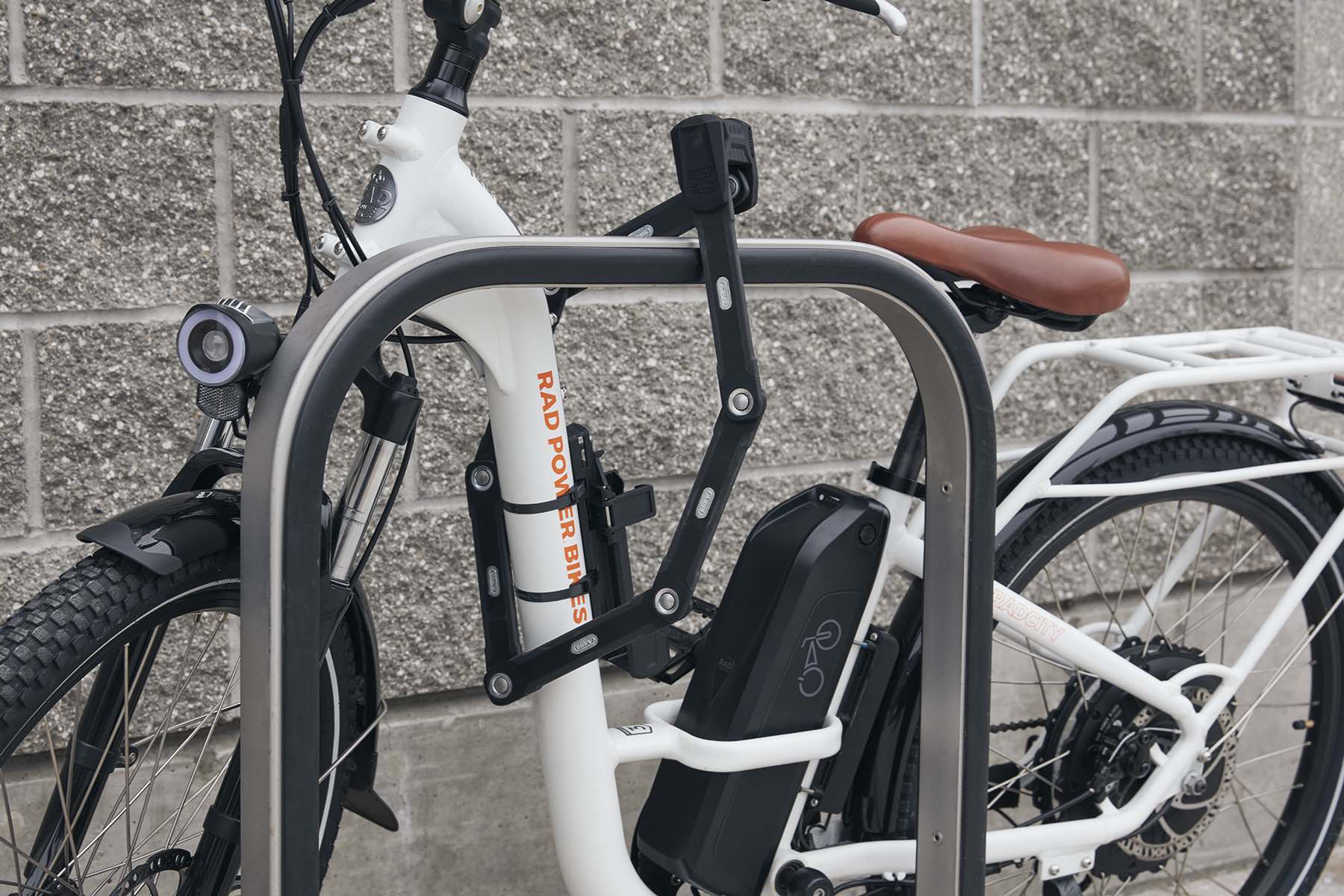 A white electric bike with a bike lock through its frame connecting it to a bike rack.