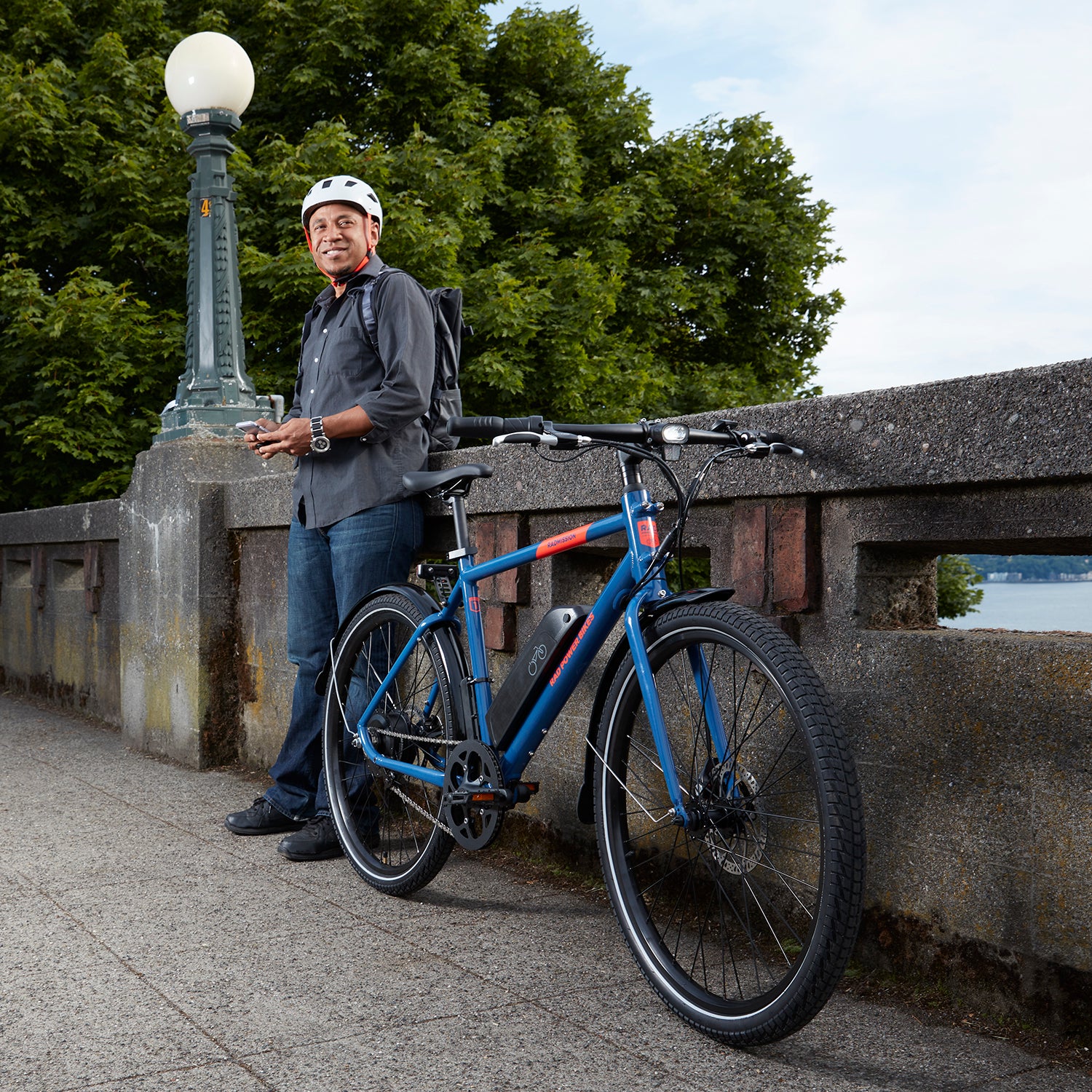 Man and his Rad Power Bike stand next to a bridge.