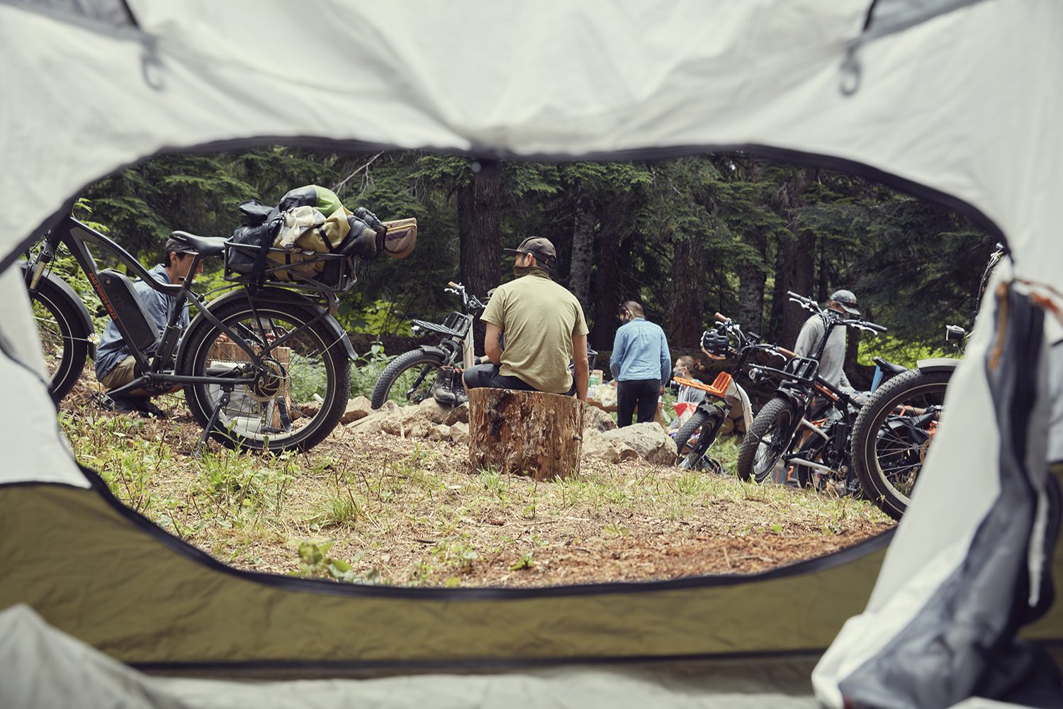 Looking outside a tent, we can see several people camping with their ebikes from Rad Power Bikes.