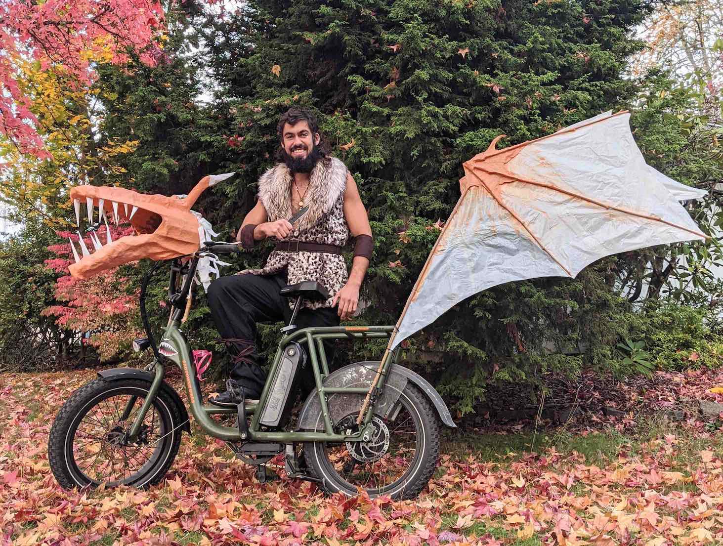 A man in a barbarian costume stands next to a RadRunner decorated to look like a dragon.