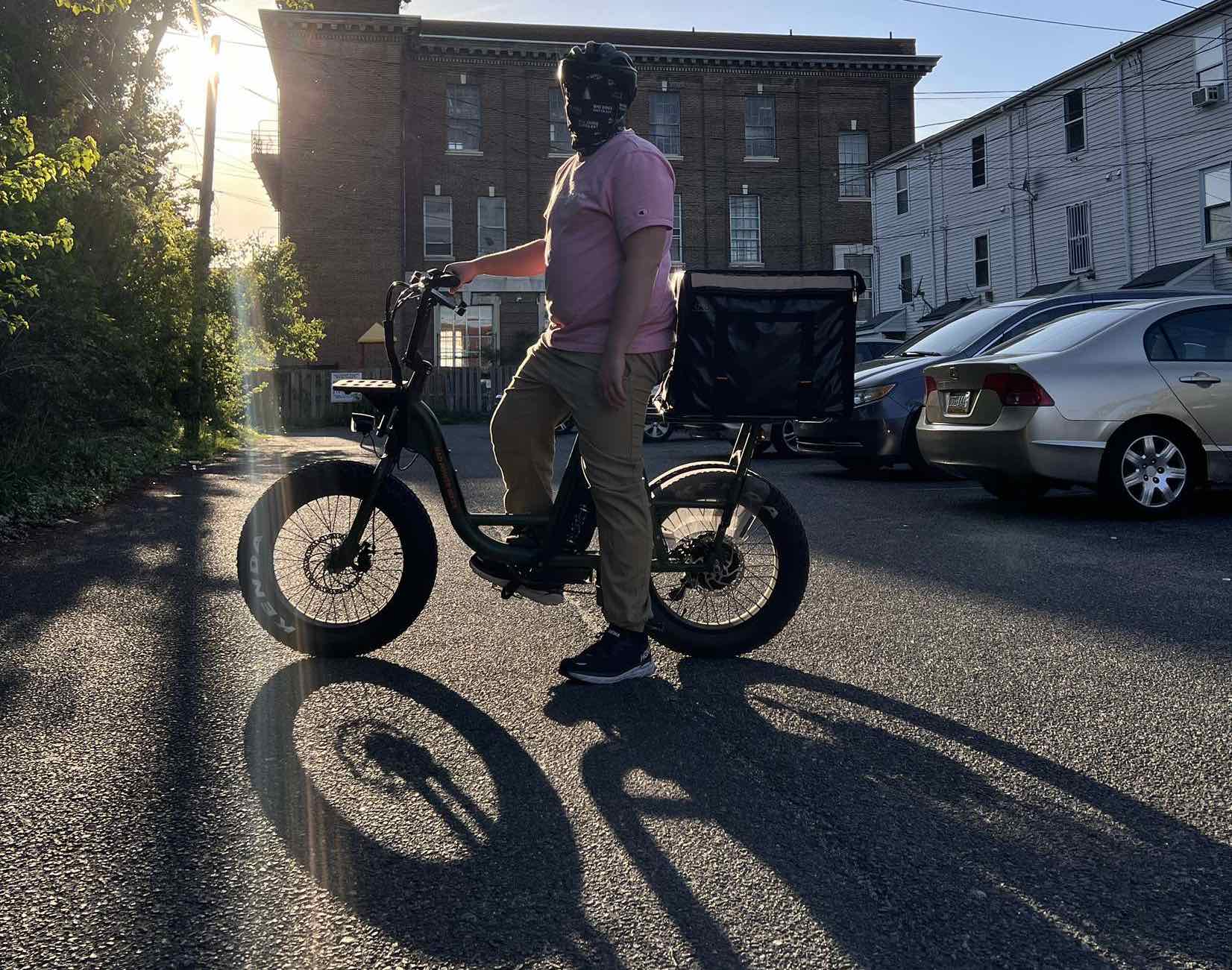 Jay, a bike courier, poses in a parking lot with a RadRunner. He is silhouetted by the afternoon sun.