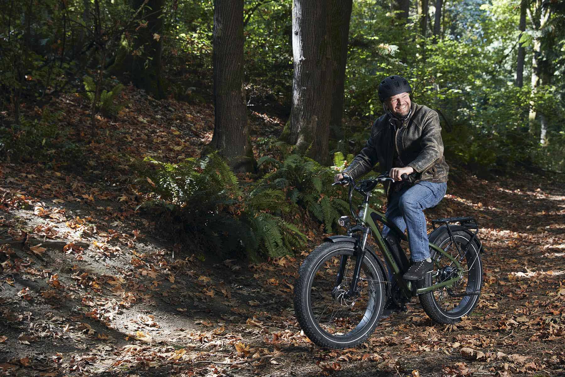 A man rides his green RadRover electric fat bike across a trail in the woods.