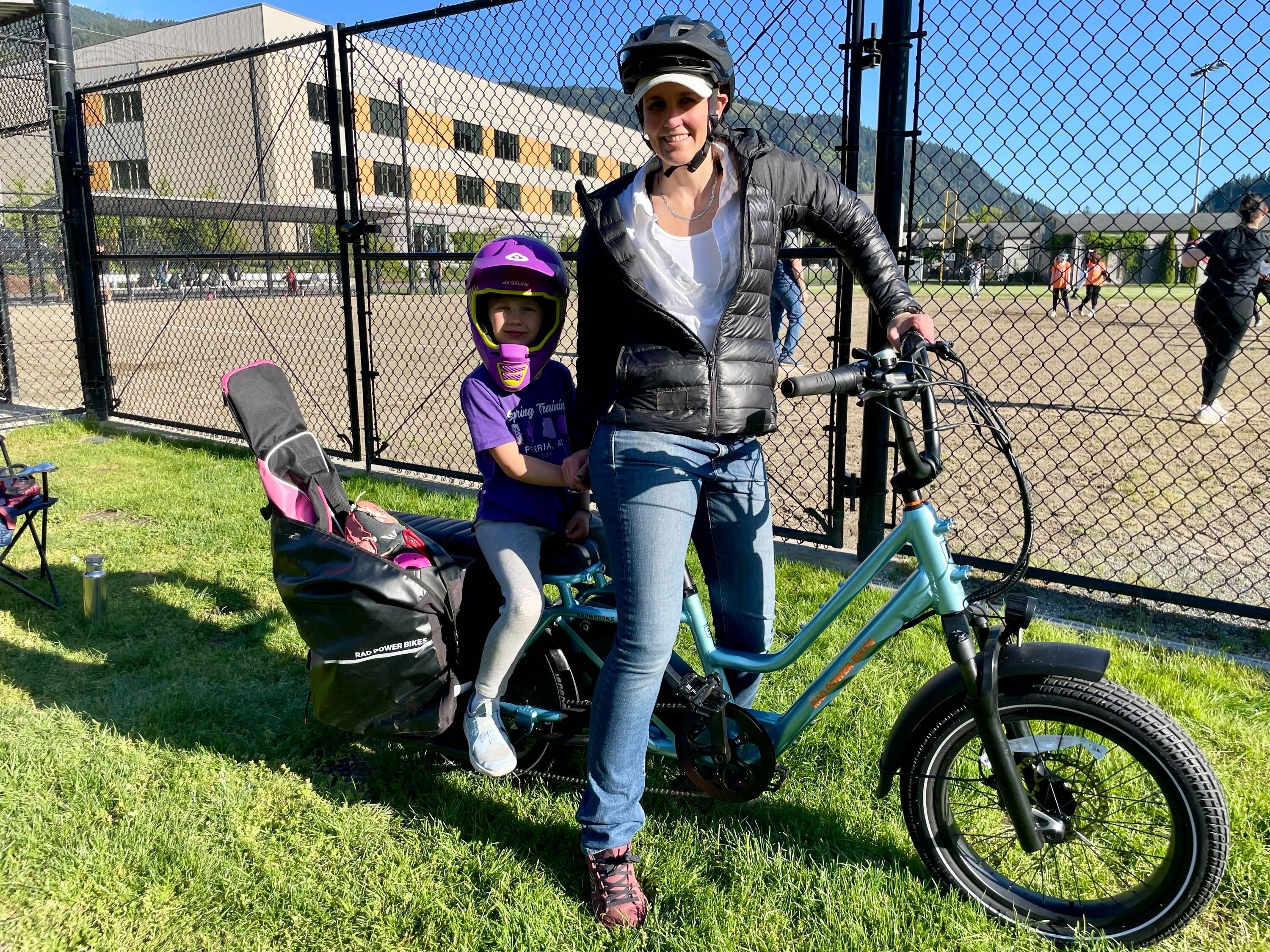 Sarah Bruce Courtney poses with a RadWagon 5 alongside her daughter outside a baseball diamond.