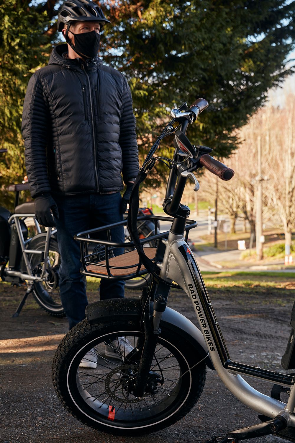 Man stands next to his ebike and wears jacket, gloves, helmet and face covering.