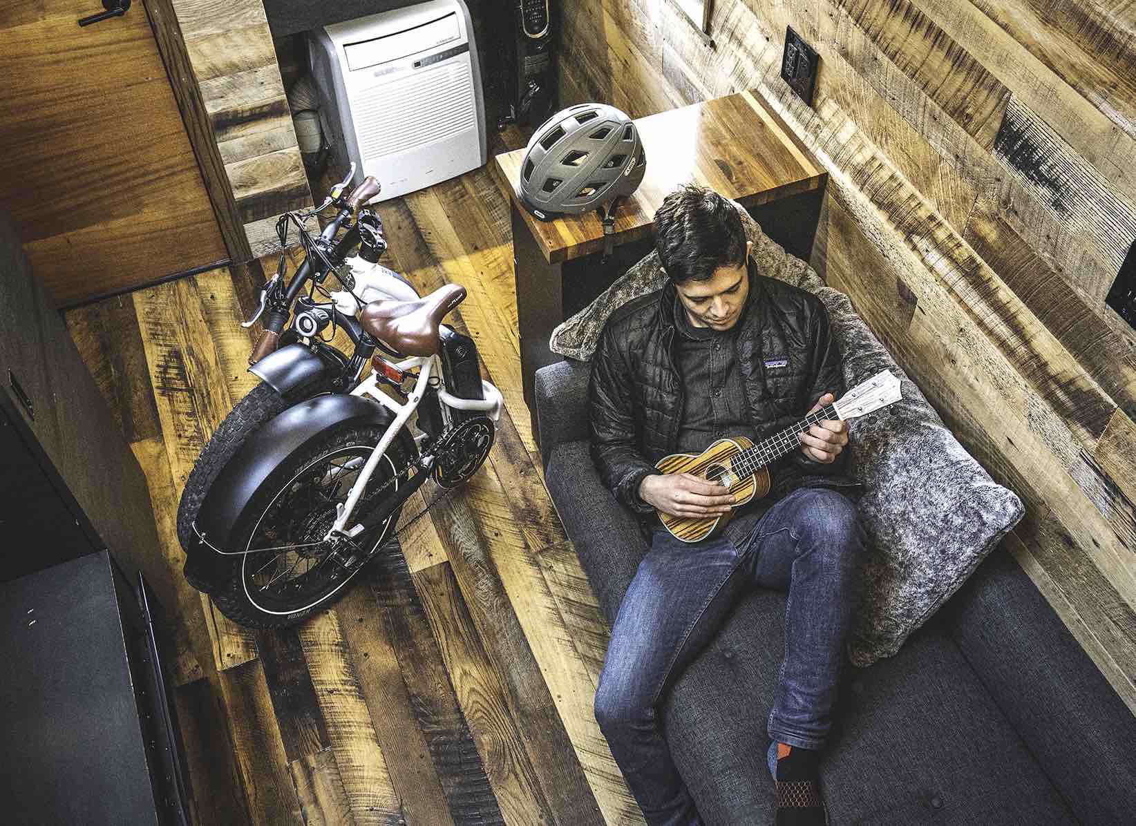 A college student plays a ukulele on a couch next to a folded up RadMini