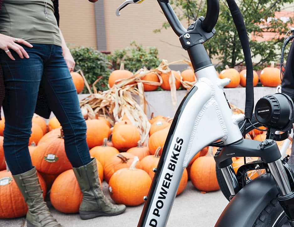 A woman stands next to a silver RadRunner Plus next to a pile of pumpkins