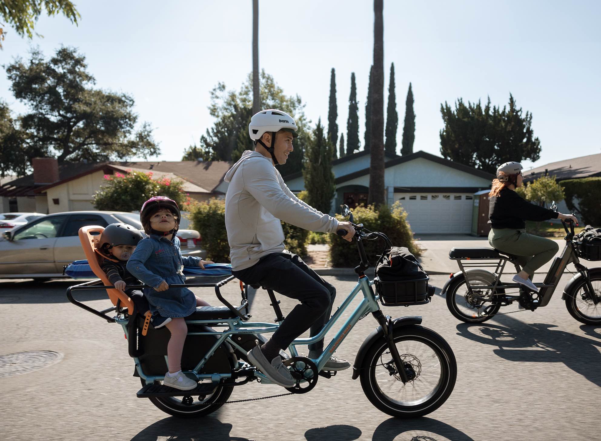 A father rides on a suburban street with two children on the back of his RadWagon 5.