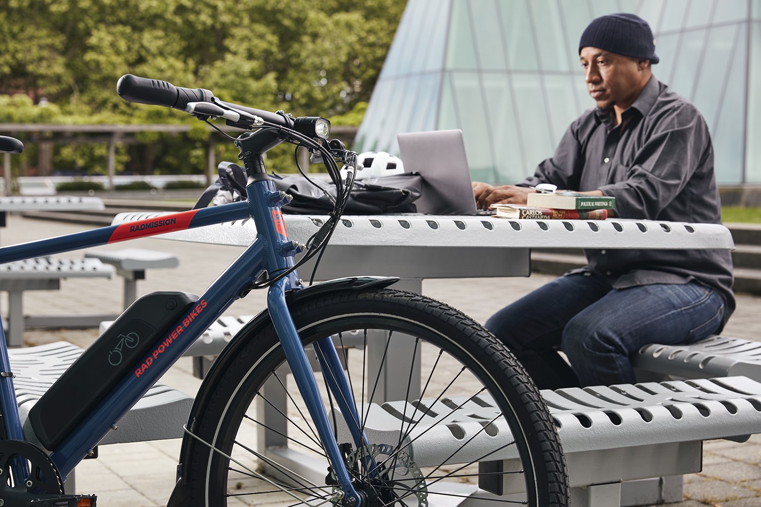 A student works at a park bench alongside a blue electric hybrid bike.