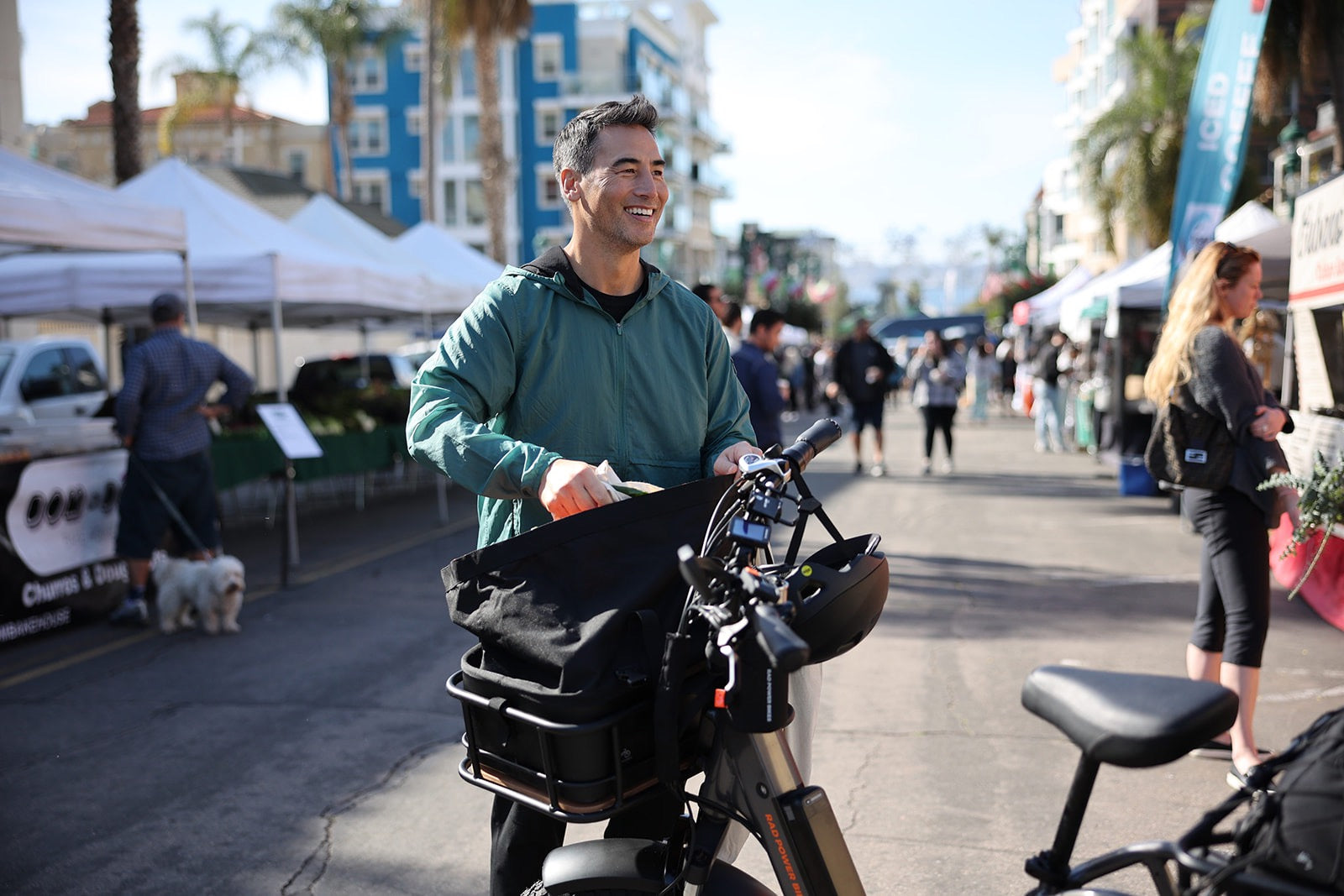 A man loads groceries into the front basket of his RadRunner 3 Plus during a sunny day at the farmer's market.