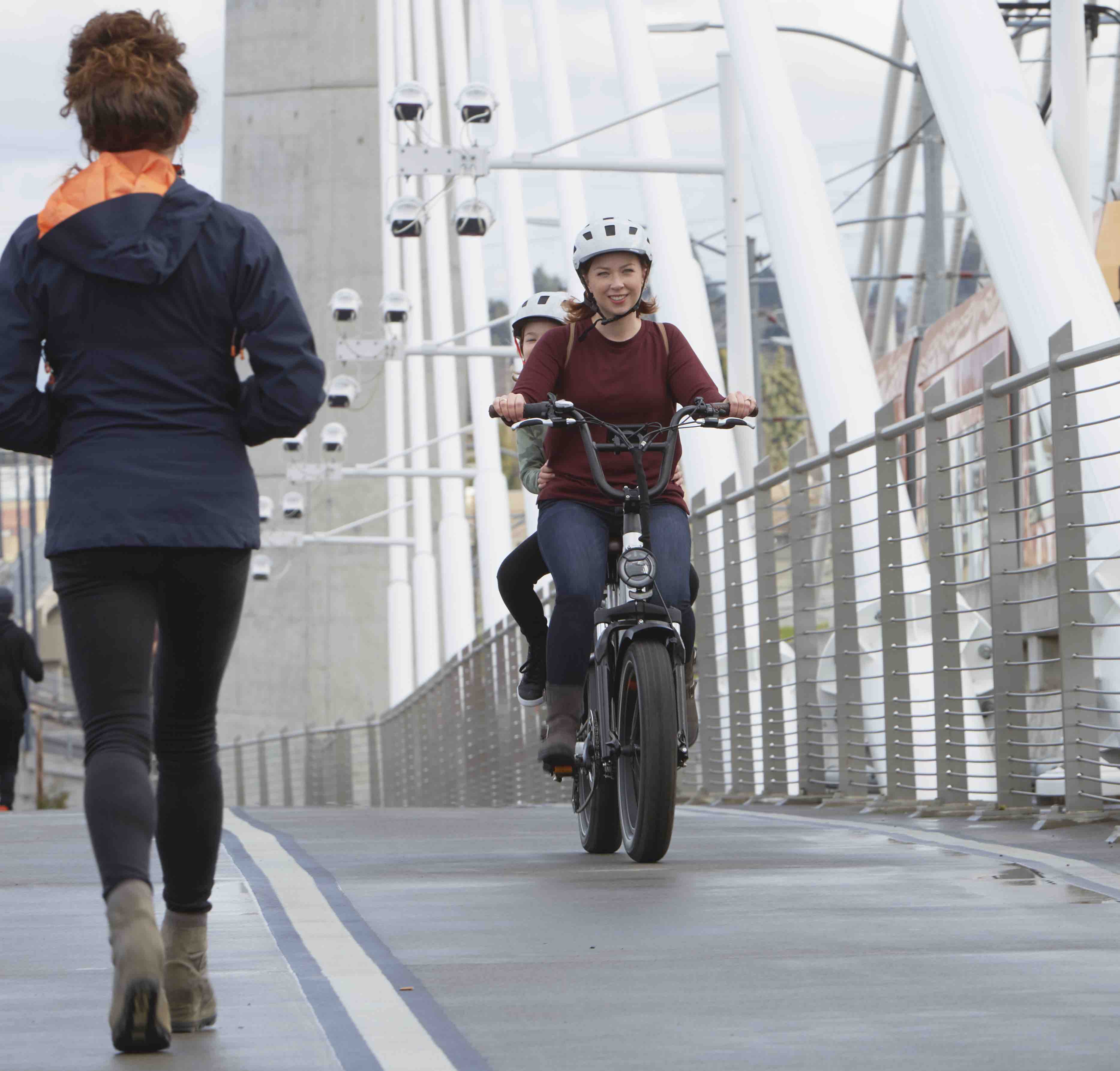 A woman and her child ride a RadRunner Plus utility ebike over a bridge on a foggy day.