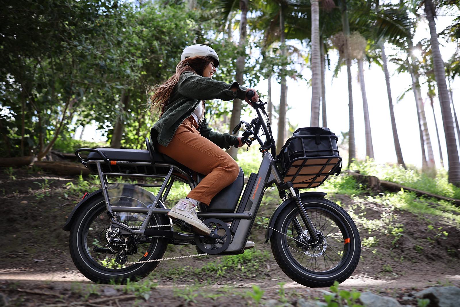 A side profile shot of a woman riding a RadRunner 3 in a tropical setting during the day. 