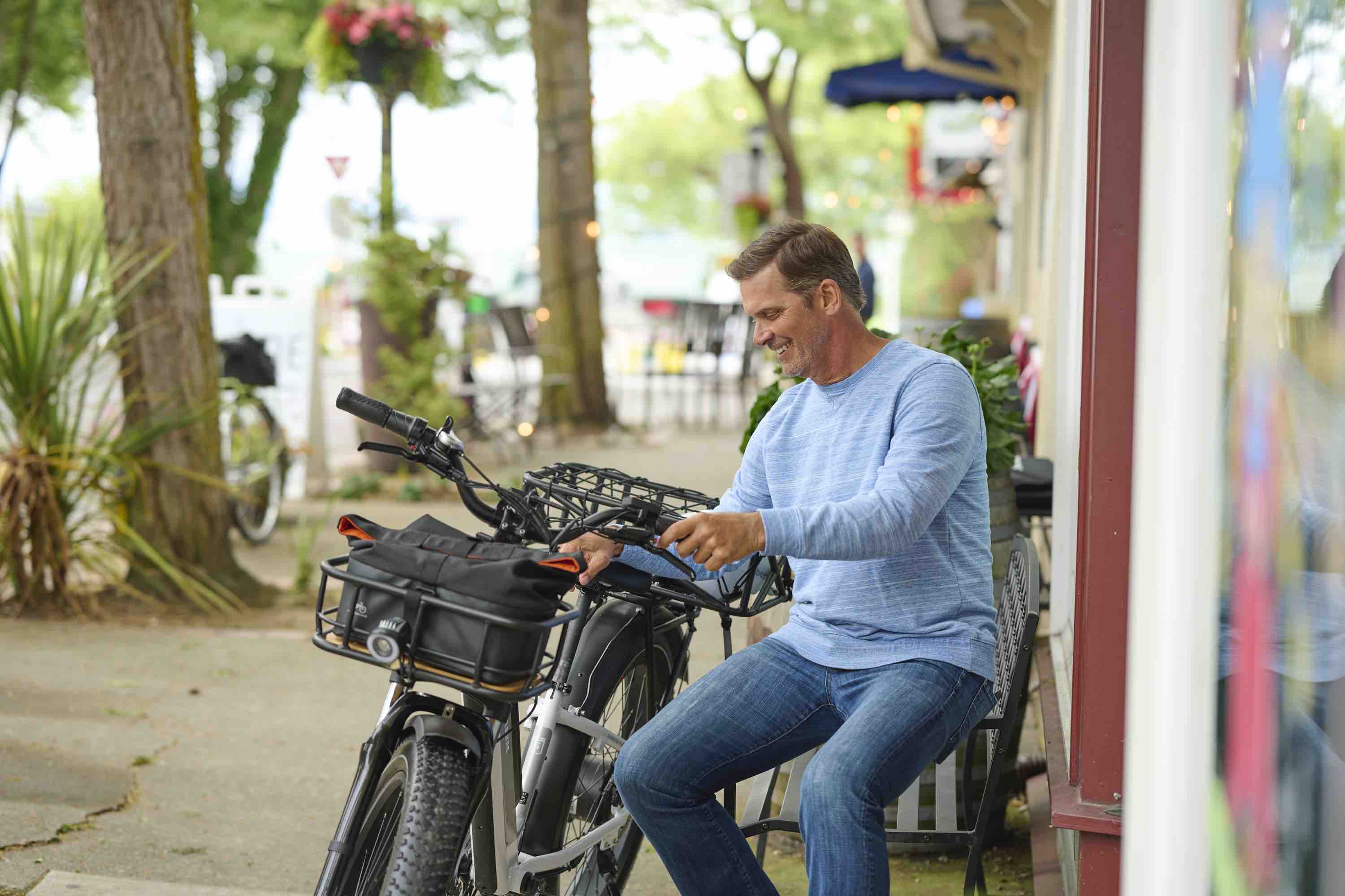 A man sits on a park bench in a small town alongside a RadRover 6 plus. He smiles as he examines it.