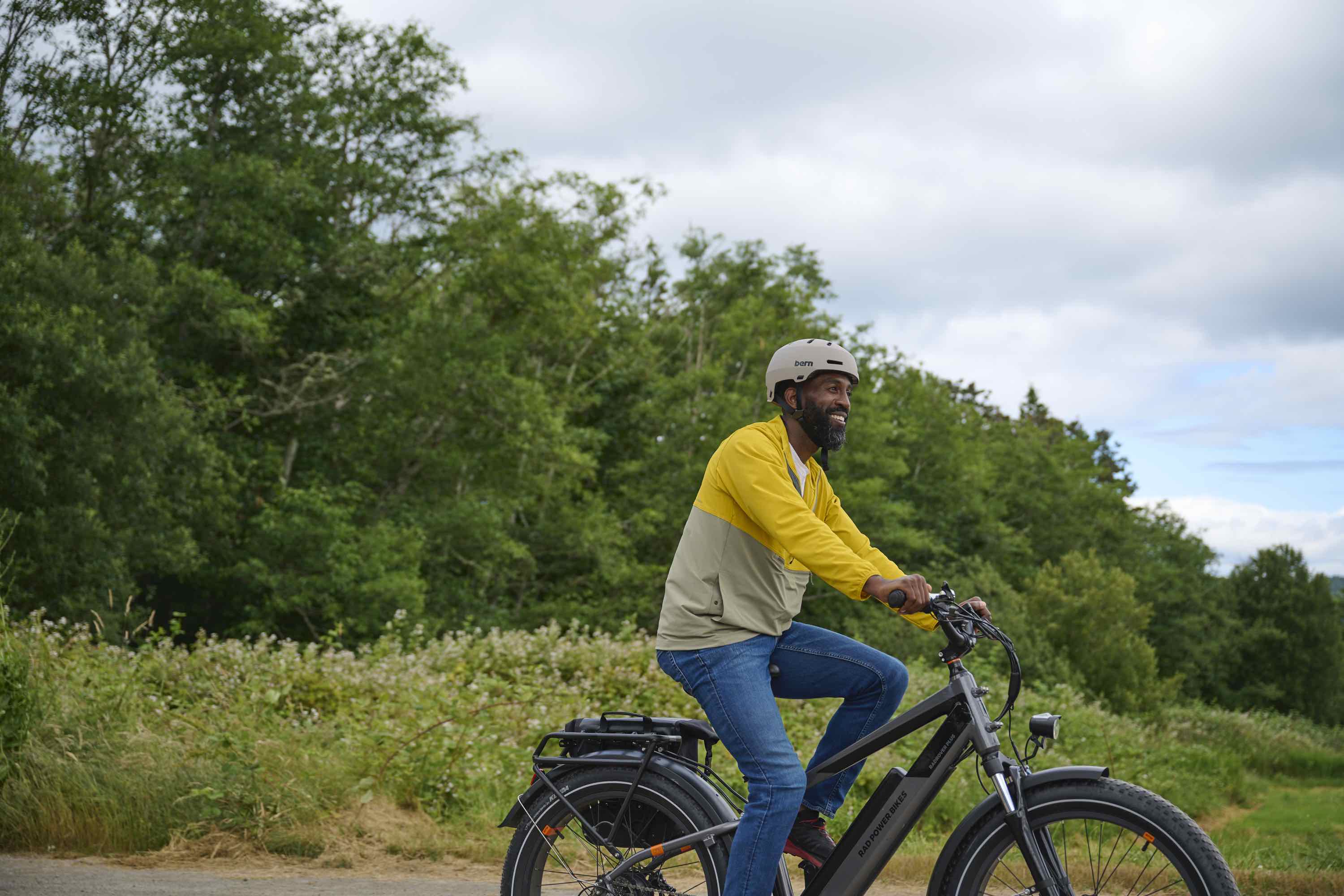 A man rides his RadRover on a rural stretch of road on a sunny day.