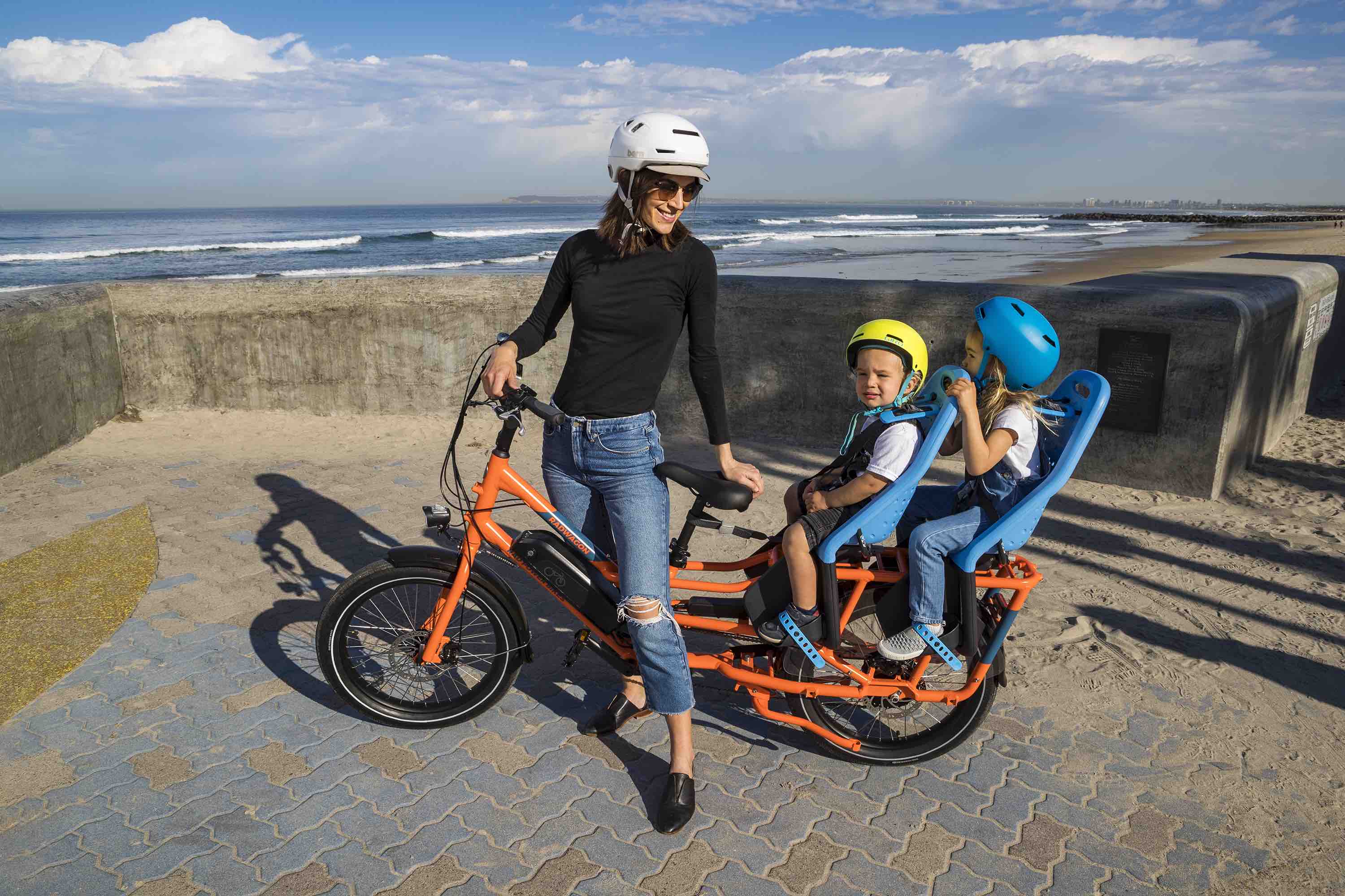 A woman rides her RadWagon by the San Diego coast with her children.