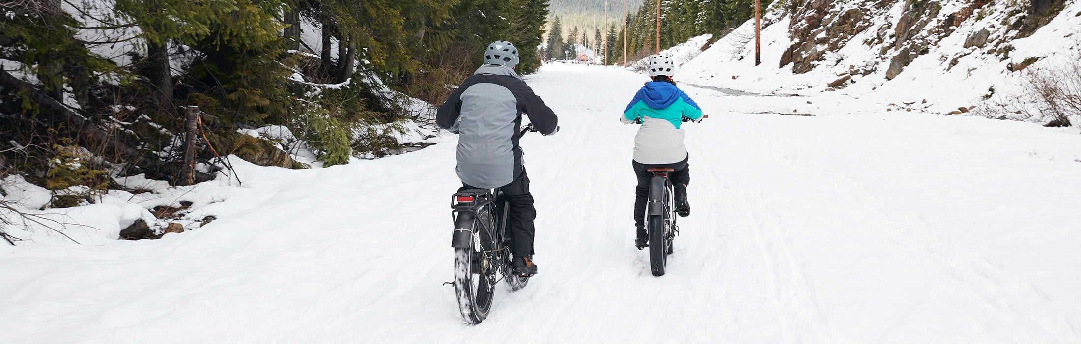 Two people ride RadRover electric fat bikes through the snow.