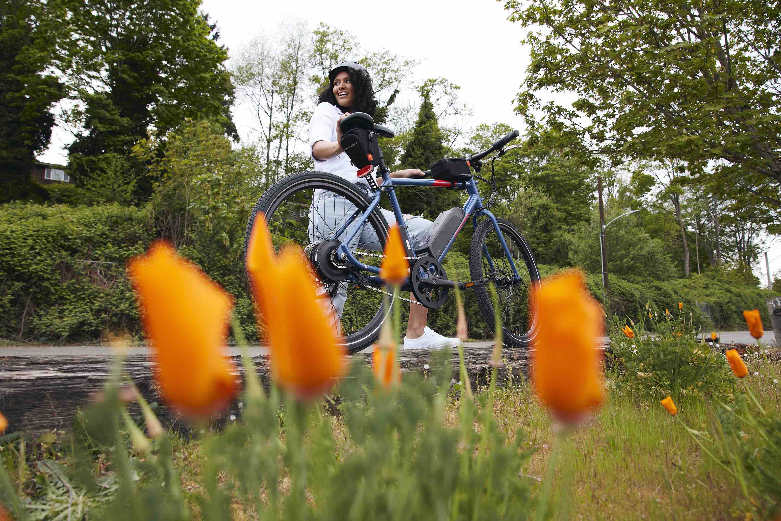 A woman poses next to her RadMission electric metro bike alongside spring flowers.