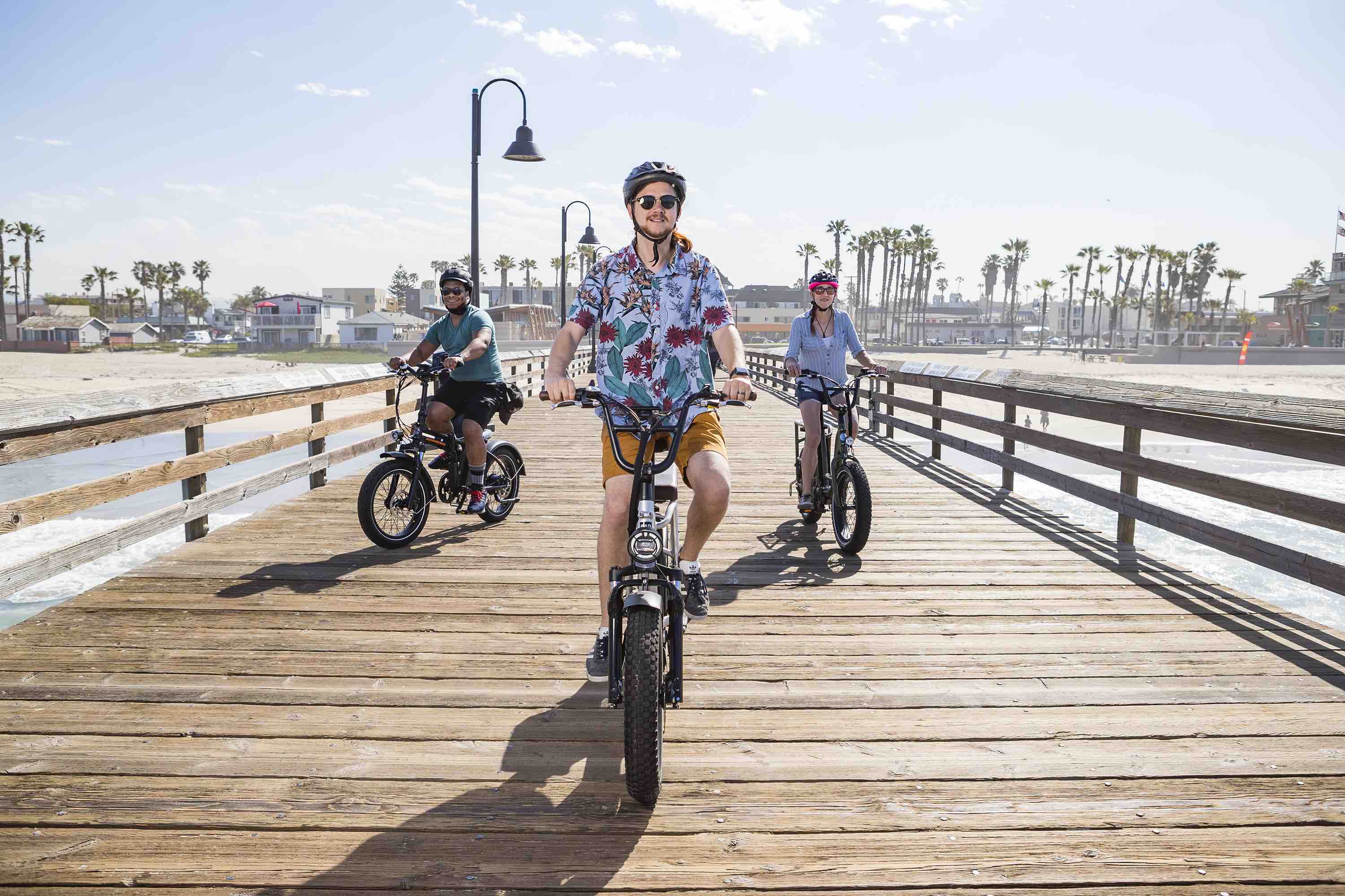 Three riders on their RadRunner electric utility bikes on a San Diego pier.