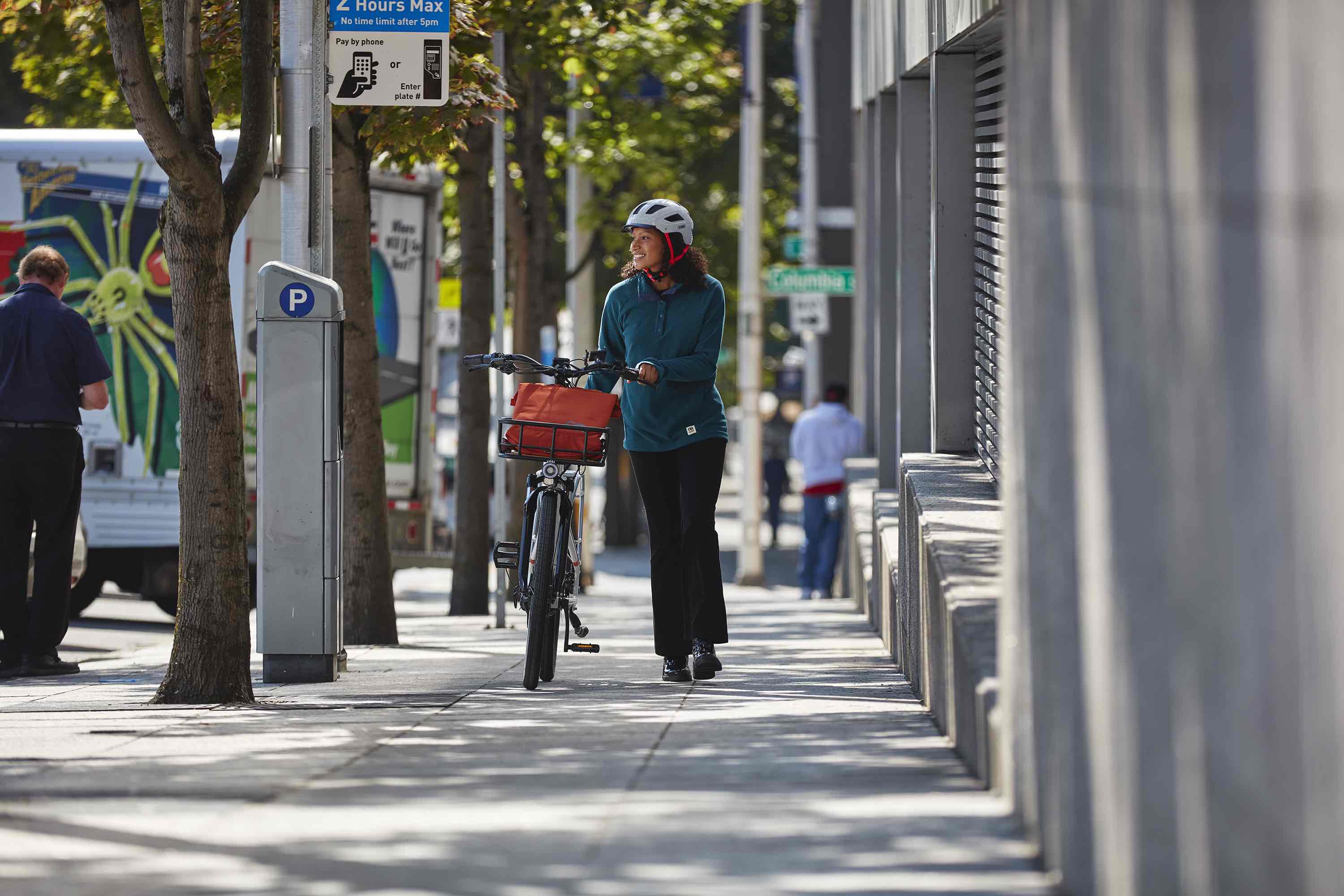 A woman walks an electric commuter bike down a city street.