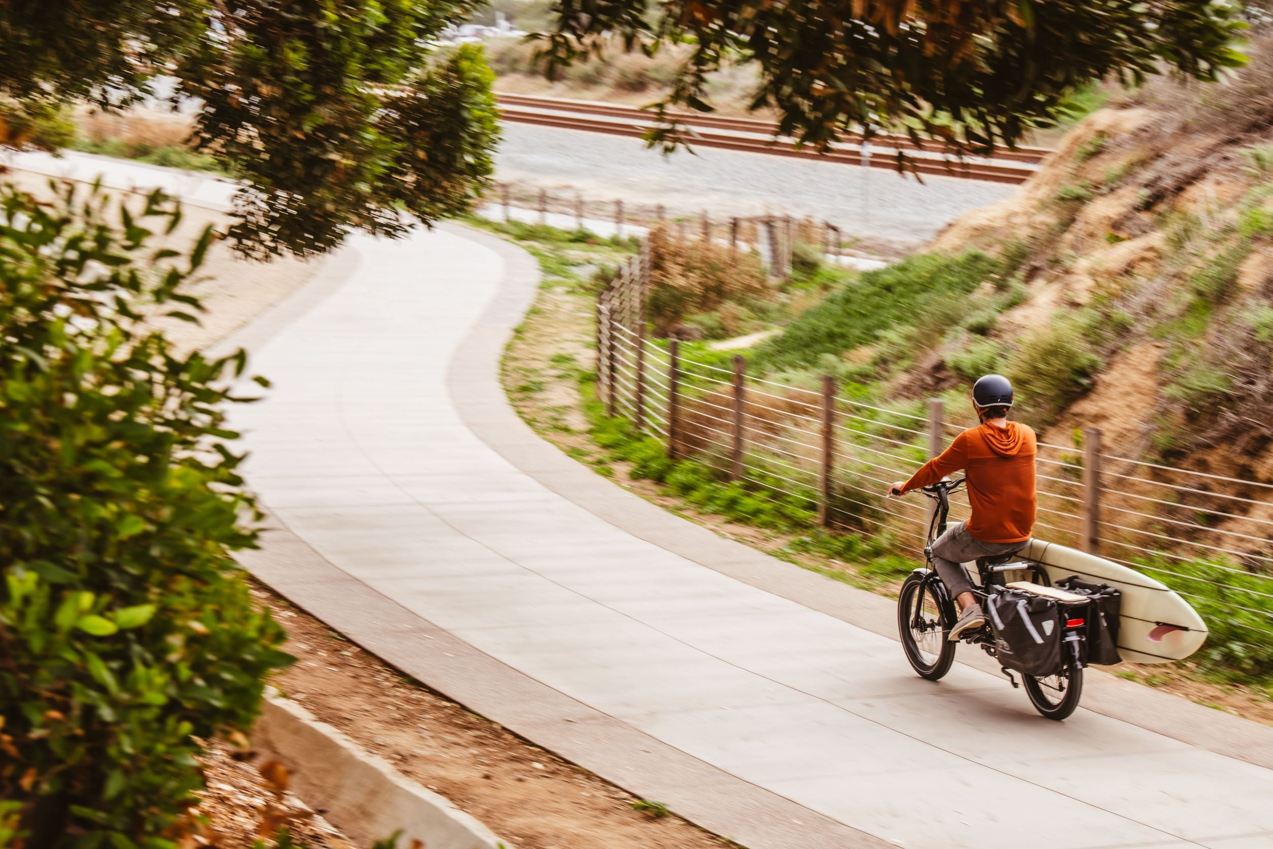 Man rides down a path on electric bike that carries a longboard.