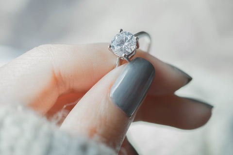 Image of woman's hand holding a diamond solitaire ring.