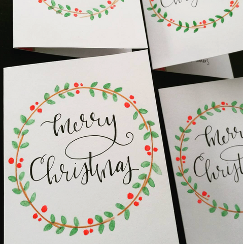 christmas card with merry christmas written in calligraphy and a colorful wreath