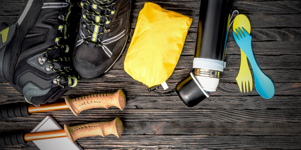 overhead flatlay image of an assortment of hiking gear sprawled across a dark natural wood floor