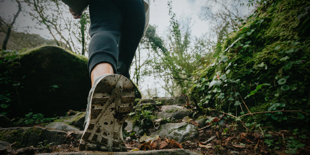 low-angle image of a the bottom of a hiker's shoe tread as they ascend an incline in the woods