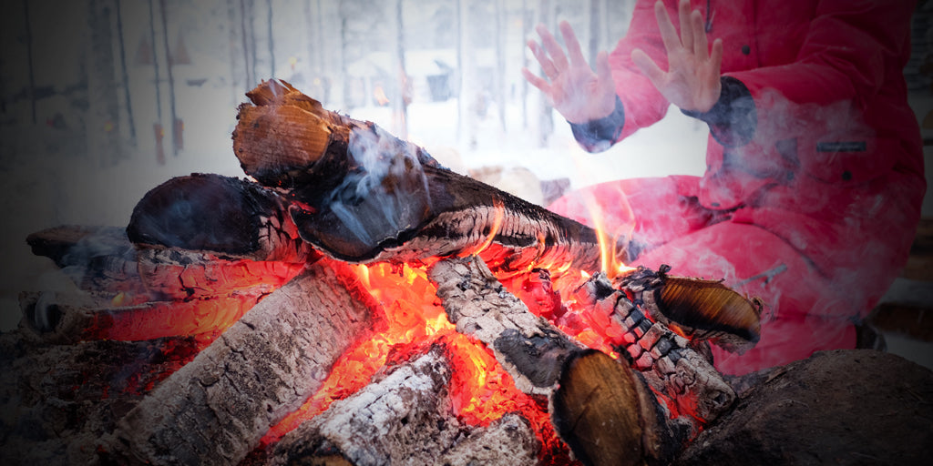 image of woman in a red ski suit with her hands stretched out towards a warm campfire in the midst of a winter storm