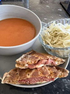 A toasted snack filled with meat and cheese served with tomato soup and salad