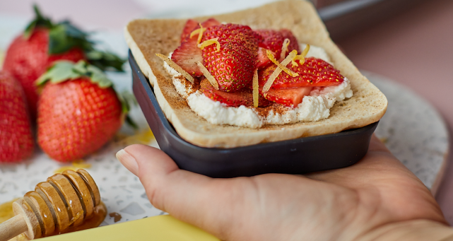 A person holding a snack filled with strawberries and cream