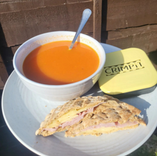 A toasted snack with cheese and ham filling served with tomato soup